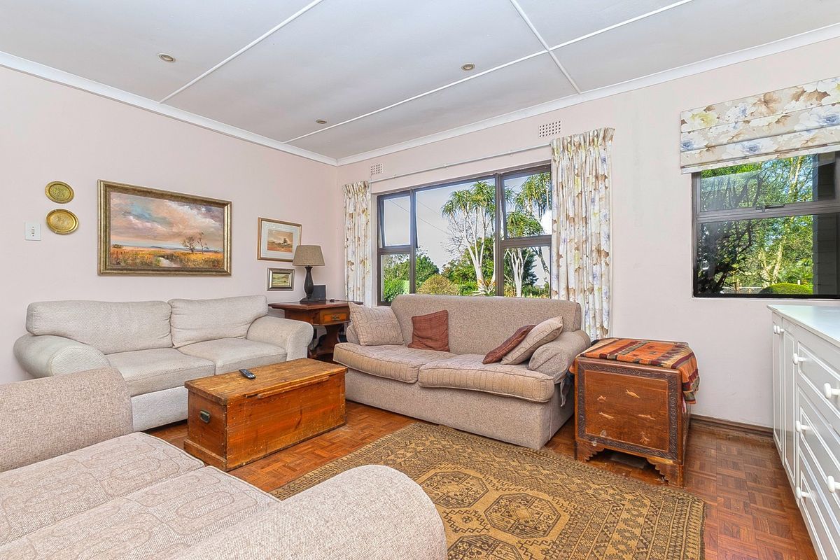 A comfortable living room featuring classic parquet flooring, recessed lighting, and large windows that provide natural light and garden views.