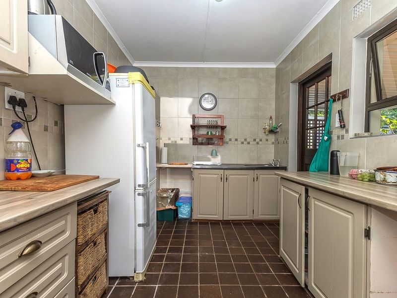 A functional kitchen featuring tiled splashbacks, laminate countertops, built-in cabinetry, and direct access to the exterior via a timber-framed door.