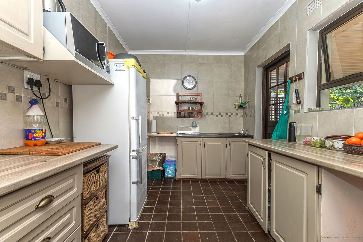 A functional kitchen featuring tiled splashbacks, laminate countertops, built-in cabinetry, and direct access to the exterior via a timber-framed door.