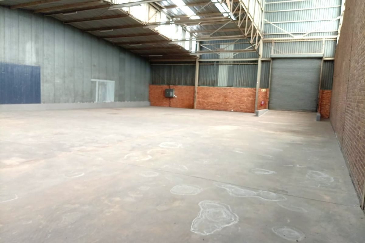 Spacious industrial warehouse unit featuring high ceilings with exposed steel trusses, concrete flooring, and a large roller shutter door for easy access.