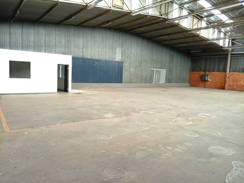 Spacious industrial warehouse featuring concrete flooring, high-clearance steel roof trusses with skylights, and an integrated internal office partition.