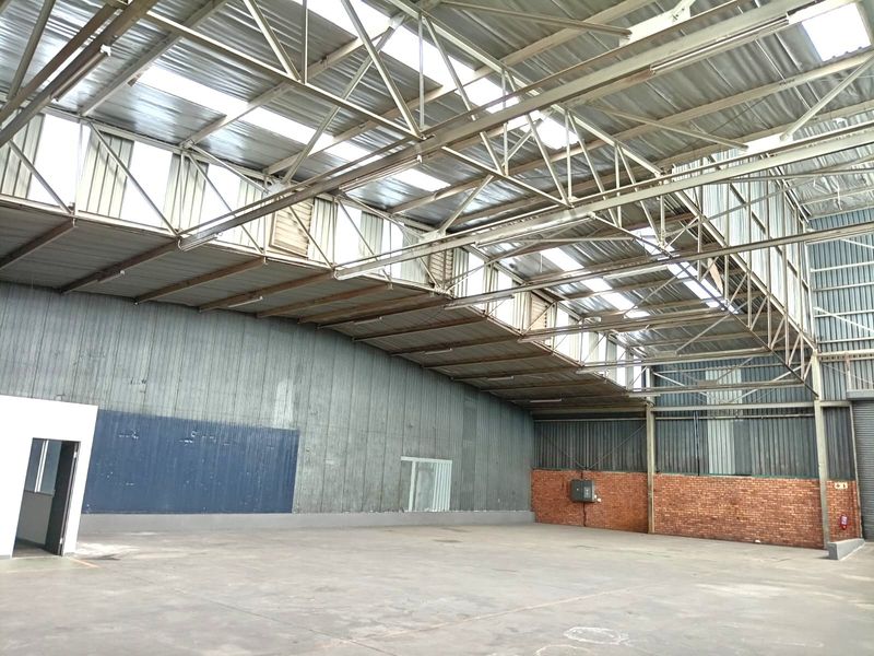 Spacious industrial warehouse interior featuring high-clearance steel truss roofing, integrated skylights, concrete flooring, and a combination of corrugated metal and brick wall finishes.
