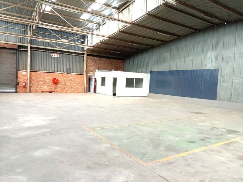 Spacious industrial warehouse featuring high-clearance steel truss roofing, concrete flooring, an internal office pod, and a large roller shutter door for easy access.