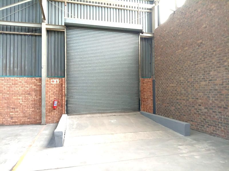 Industrial loading bay area featuring a large roller shutter door, concrete loading ramp, and durable brick and metal wall construction.