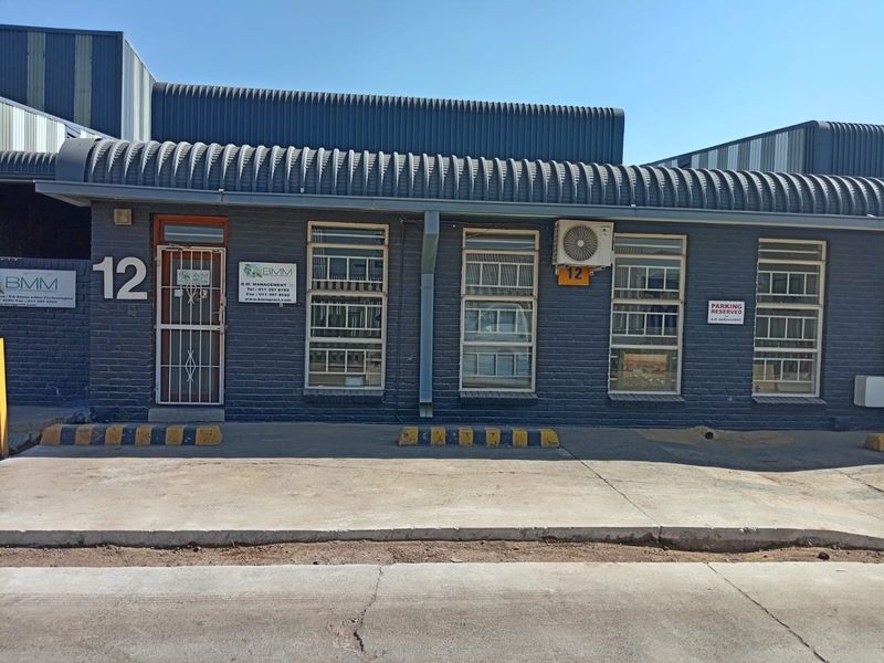 Front facade of a commercial unit featuring a brick exterior, metal security gate, and dedicated parking area with concrete driveway.
