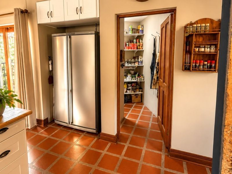 A functional scullery area featuring terracotta tiled flooring, built-in cabinetry, and a convenient walk-in pantry with shelving.