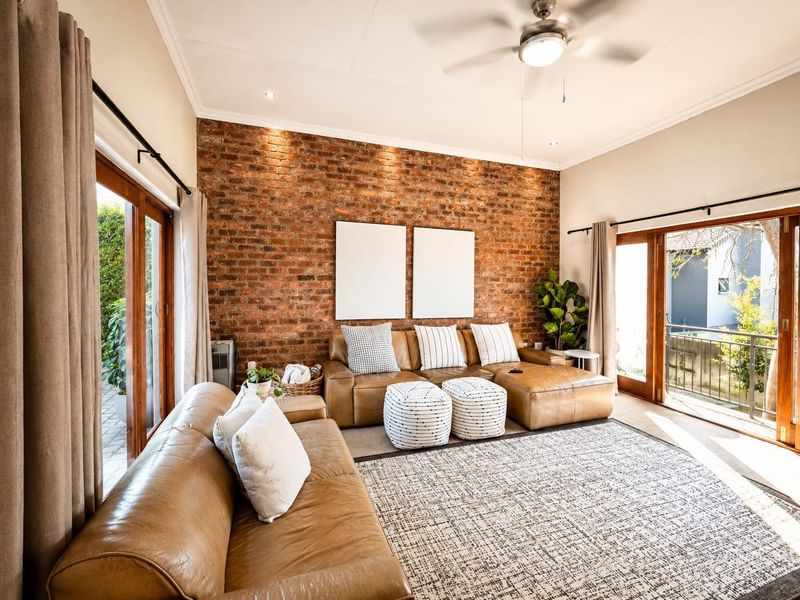A bright living room featuring an exposed brick feature wall, ceiling fan, and dual sliding glass doors providing access to outdoor areas.