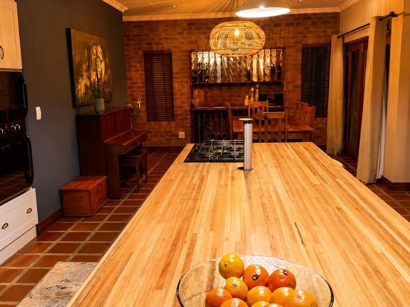 Spacious open-plan kitchen and dining area featuring a large butcher block island, gas cooktop, exposed brick walls, and warm terracotta flooring.