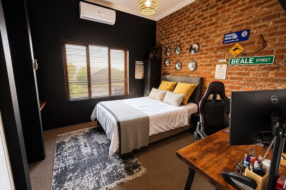 A well-maintained bedroom featuring an exposed brick feature wall, dark accent wall, carpeted flooring, and a wall-mounted split-system air conditioner.