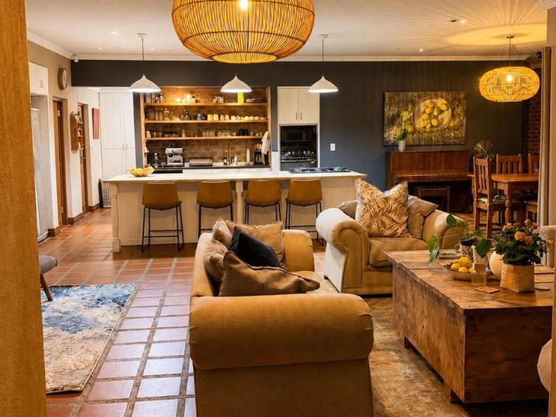 Spacious open-plan living area featuring terracotta tile flooring, a central kitchen island with breakfast bar, and warm ambient pendant lighting throughout.