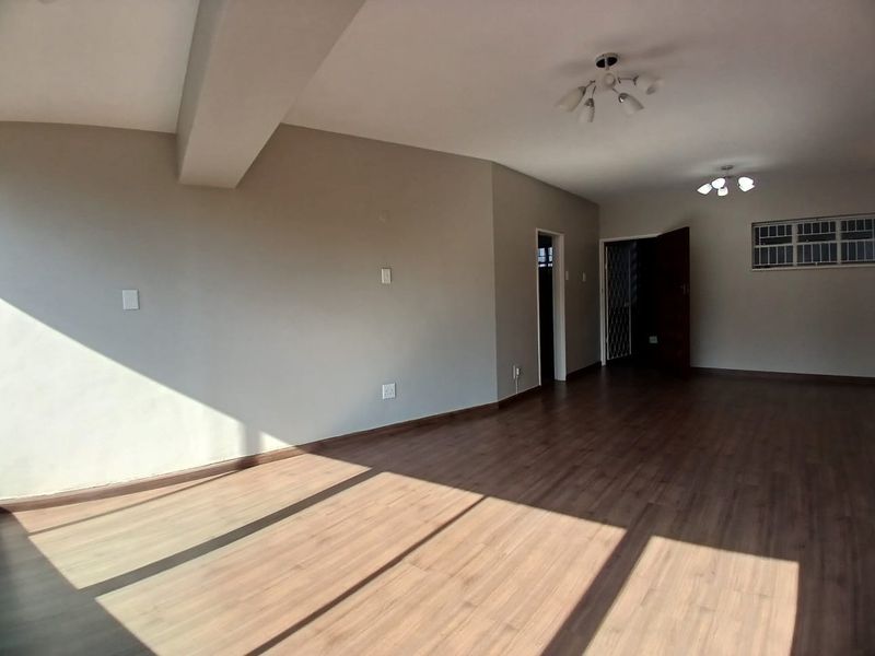 A spacious, empty living area featuring modern laminate flooring, neutral wall tones, and multiple ceiling light fixtures, offering a blank canvas for interior design.