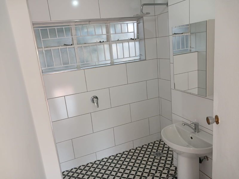 A clean, modern bathroom featuring white subway-style wall tiles, patterned floor tiles, a pedestal basin, and a shower area.