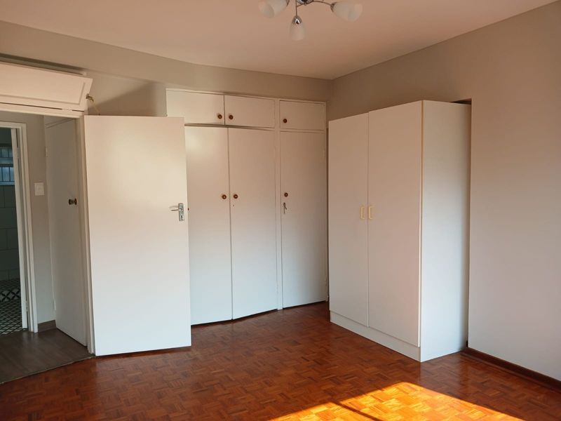 A bright bedroom featuring classic parquet flooring and extensive built-in cupboard storage, providing a clean and functional space ready for personalization.