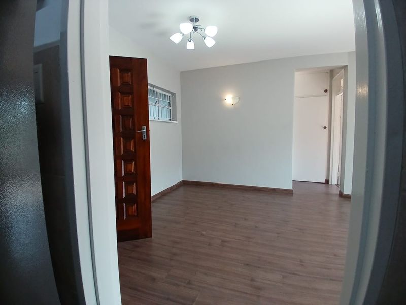 A bright, empty living area featuring laminate flooring, neutral walls, and a built-in cupboard, offering a clean and versatile space.