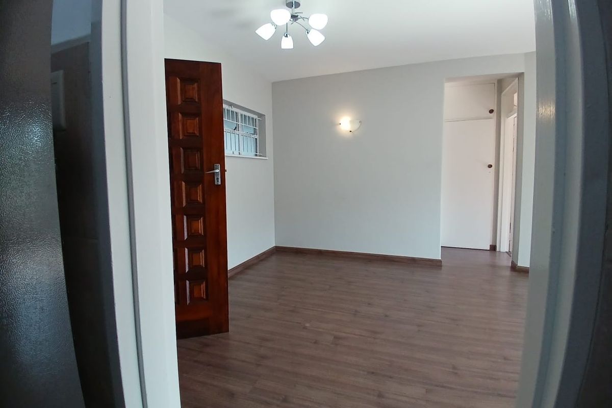 A bright, empty living area featuring laminate flooring, neutral walls, and a built-in cupboard, offering a clean and versatile space.