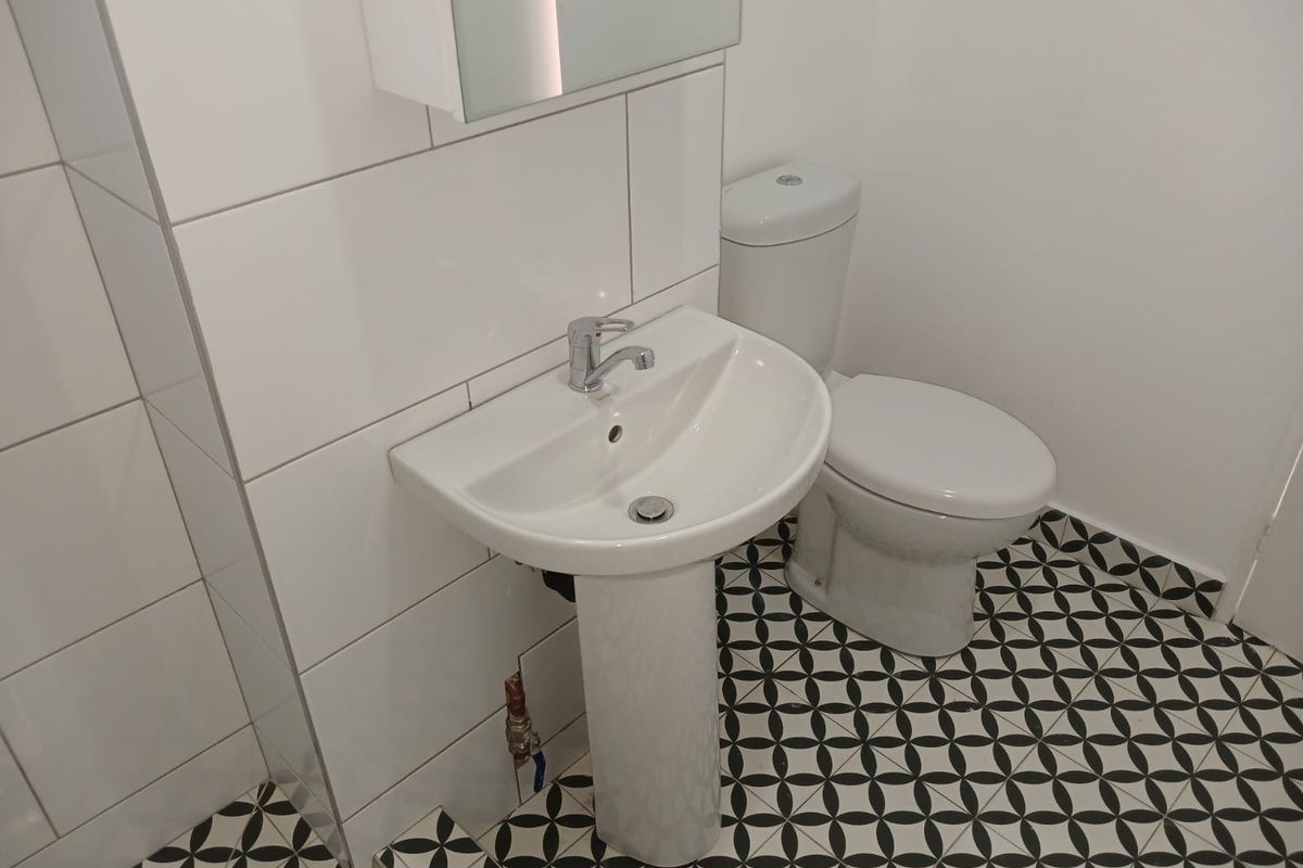 A clean, modern bathroom featuring a pedestal basin, toilet, and striking patterned floor tiles with white wall tiling.