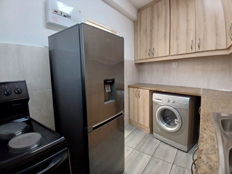 A functional kitchen featuring laminate cabinetry, tiled flooring, and integrated space for laundry appliances and a freestanding stove.