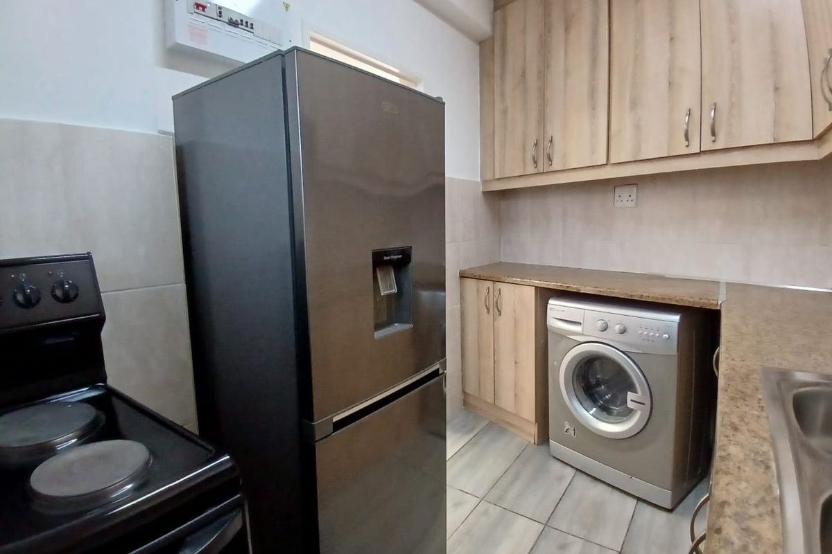 A functional kitchen featuring laminate cabinetry, tiled flooring, and integrated space for laundry appliances and a freestanding stove.