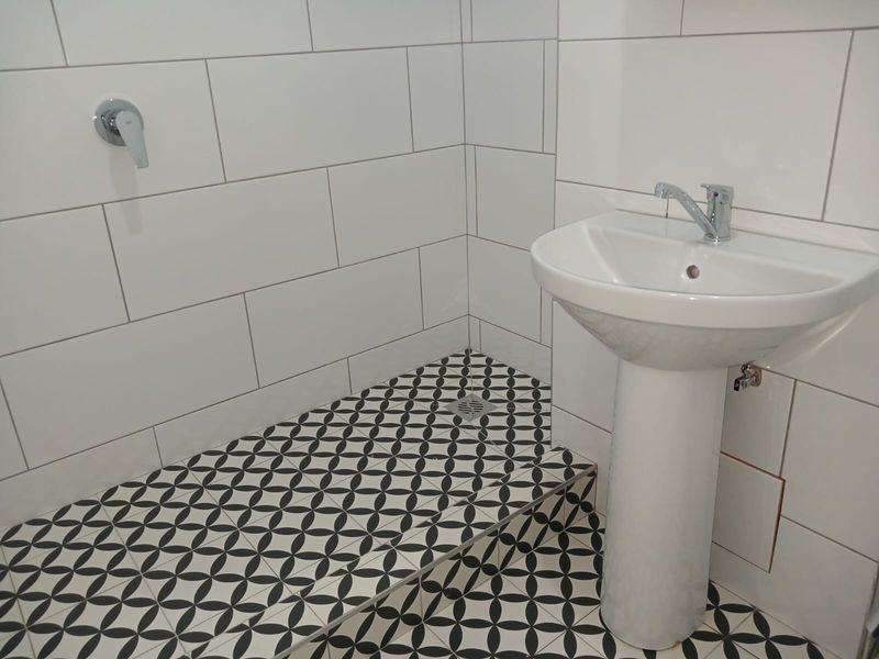 Modern bathroom featuring a walk-in shower with patterned floor tiles, white subway wall tiling, and a clean pedestal basin with chrome fixtures.