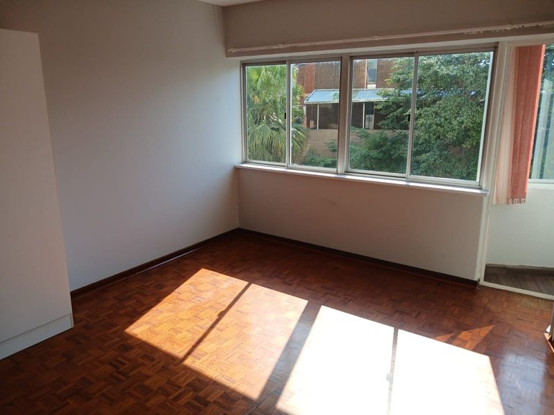 A bright, empty bedroom featuring classic parquet flooring, large sliding windows providing natural light, and a built-in cupboard.