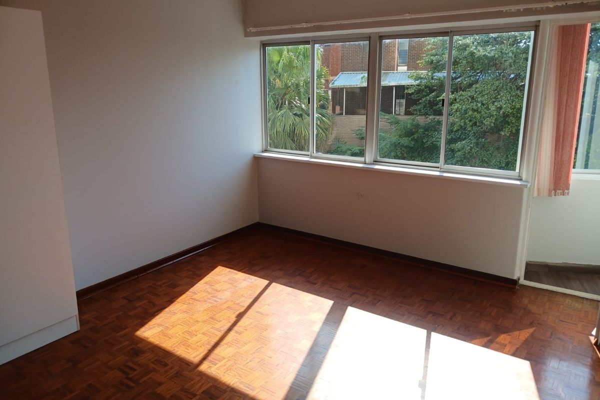 A bright, empty bedroom featuring classic parquet flooring, large sliding windows providing natural light, and a built-in cupboard.
