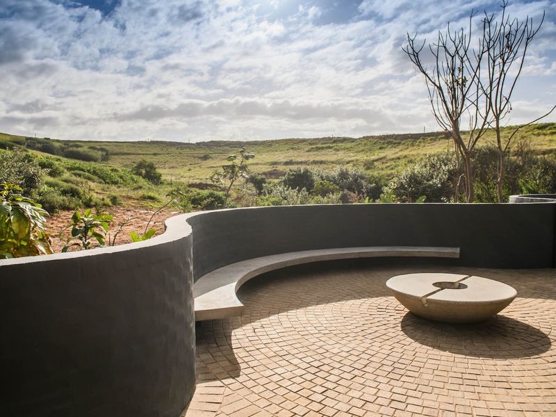 A modern outdoor patio featuring a curved concrete bench, a central stone fire pit, and scenic views of the surrounding landscape.
