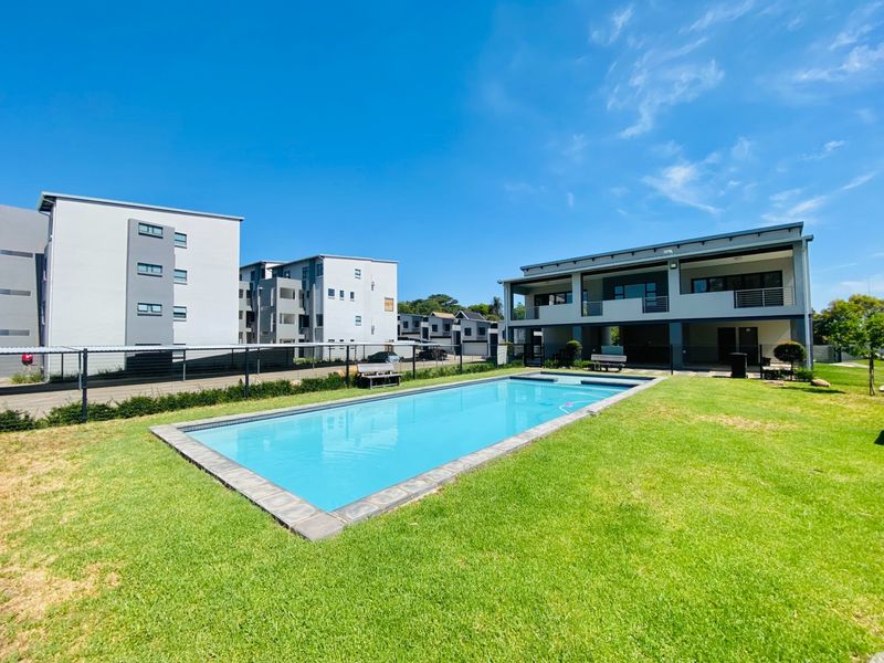 A well-maintained communal swimming pool area featuring a clear pool, stone coping, and surrounding landscaped lawn within an apartment complex.