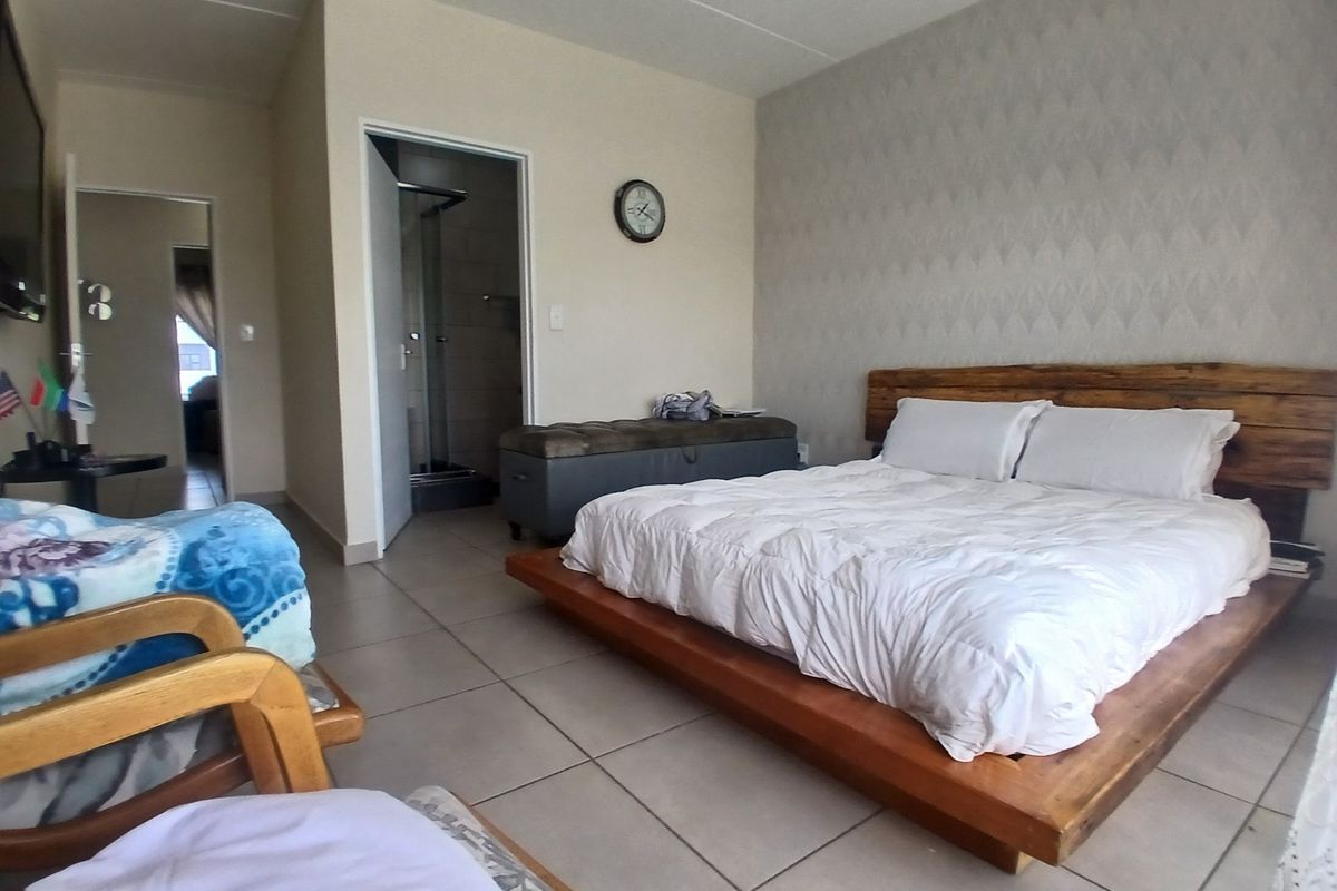 A spacious bedroom featuring tiled flooring, a textured feature wall, and direct access to an en-suite bathroom.