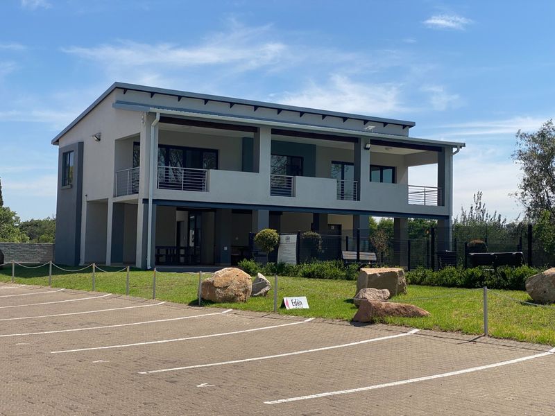 A modern two-story apartment building exterior featuring balconies with metal railings, set against a paved parking area and landscaped grounds.