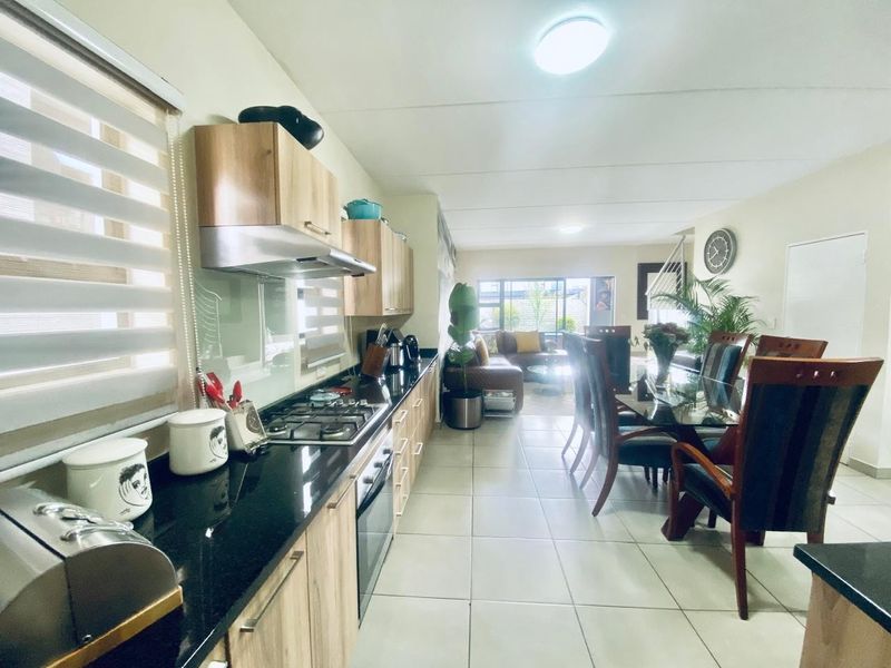 Open-plan living area featuring a modern kitchen with granite countertops, gas hob, and tiled flooring, flowing into a dining and lounge space.