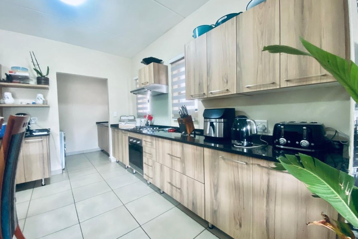 Modern kitchen featuring light wood-grain cabinetry, dark granite countertops, built-in oven, gas hob, and tiled flooring with an adjacent scullery area.