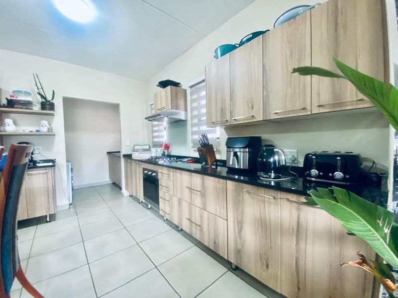 Modern kitchen featuring light wood-grain cabinetry, dark granite countertops, built-in oven, gas hob, and tiled flooring with an adjacent scullery area.