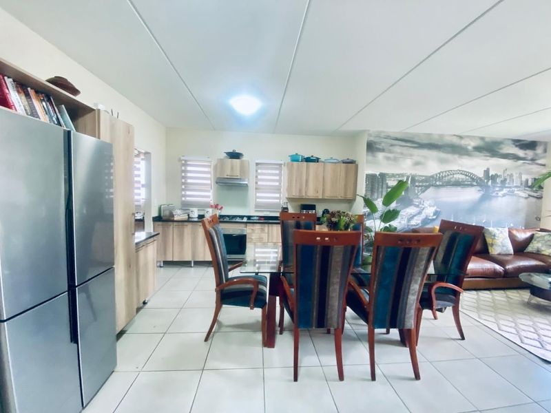 Open-plan living and dining area featuring a functional kitchen with built-in cabinetry, hob, and oven, finished with tiled flooring throughout.