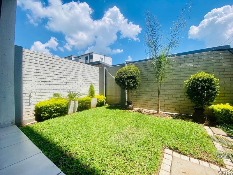 A well-maintained private garden featuring a manicured lawn, paved walkway, and painted brick boundary walls.
