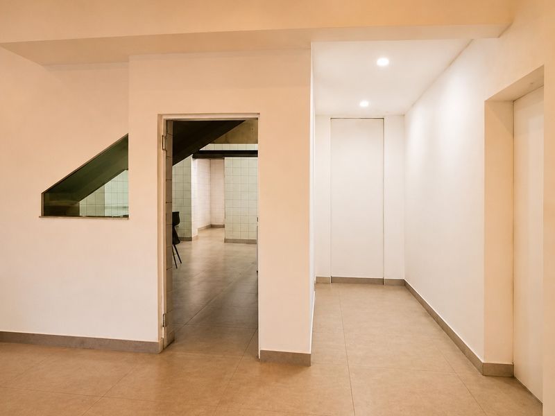 A clean, minimalist hallway featuring neutral tiled flooring, recessed lighting, and seamless flush-mounted doors leading to adjacent commercial spaces.