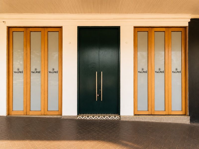 A well-maintained commercial entrance featuring a dark double door flanked by timber-framed glass panels and decorative floor tiling under a covered porch.