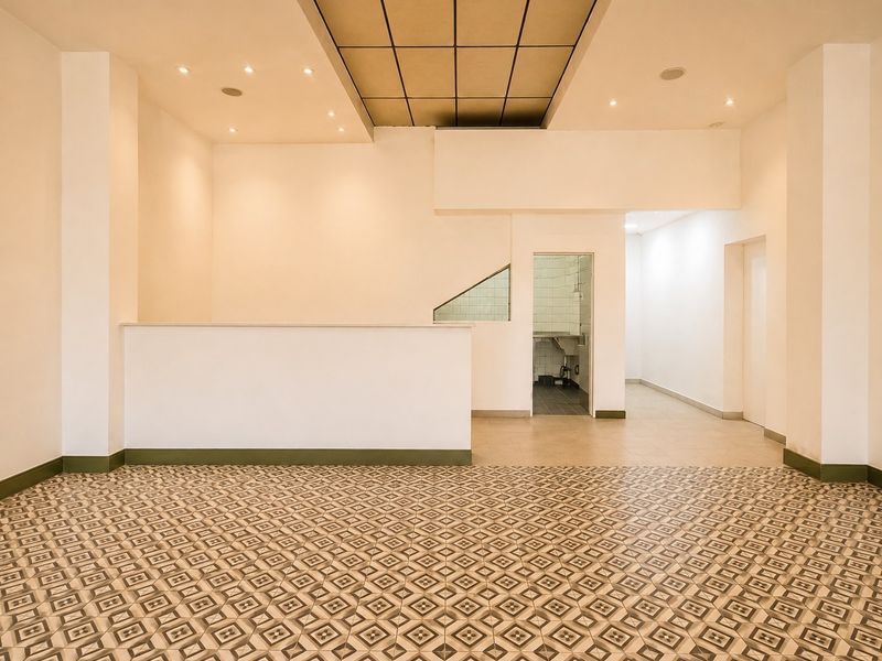 Spacious open-plan commercial area featuring decorative tiled flooring, a built-in reception counter, recessed lighting, and an adjoining tiled scullery or prep space.
