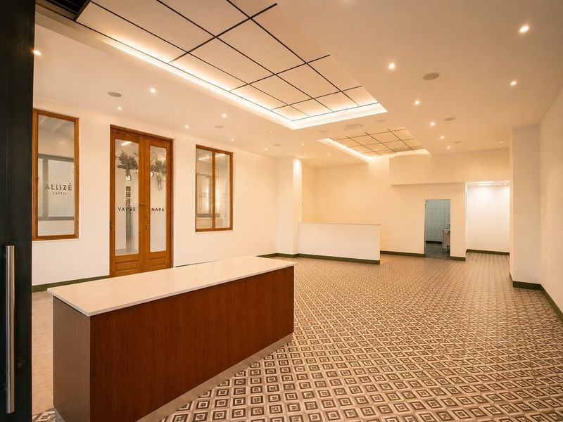 Spacious open-plan commercial interior featuring a built-in service counter, decorative patterned floor tiles, and modern recessed ceiling lighting with suspended panels.