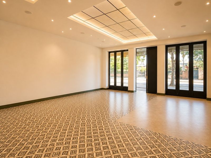 A bright, vacant commercial space featuring elegant patterned floor tiles, recessed ceiling lighting, and large glass doors providing ample natural light.