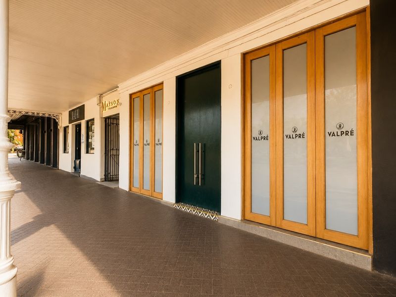 Commercial storefront entrance featuring a covered walkway, tiled flooring, and modern timber-framed glass doors with professional signage.