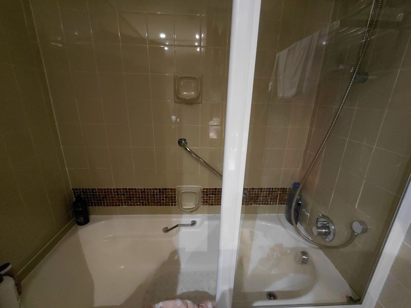 A functional bathroom featuring a built-in bathtub with a handheld shower attachment, safety grab rails, and tiled wall finishes.