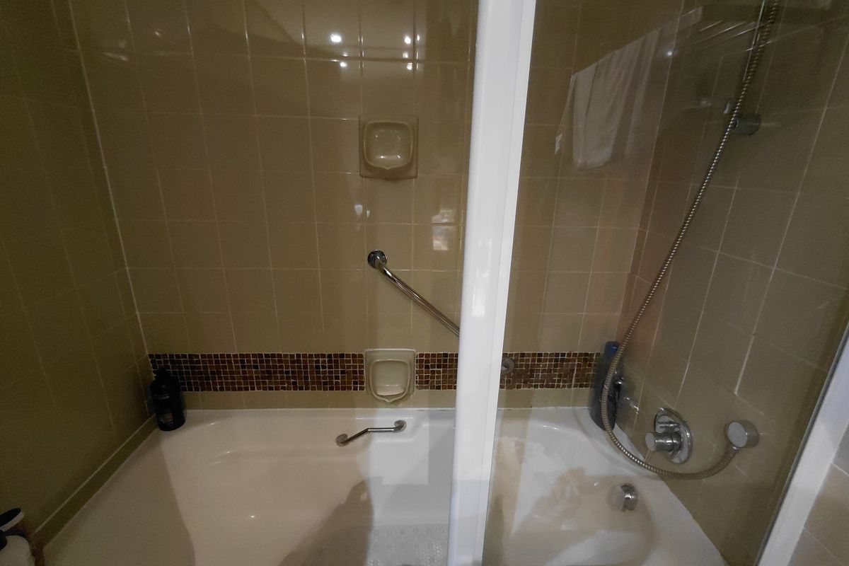 A functional bathroom featuring a built-in bathtub with a handheld shower attachment, safety grab rails, and tiled wall finishes.