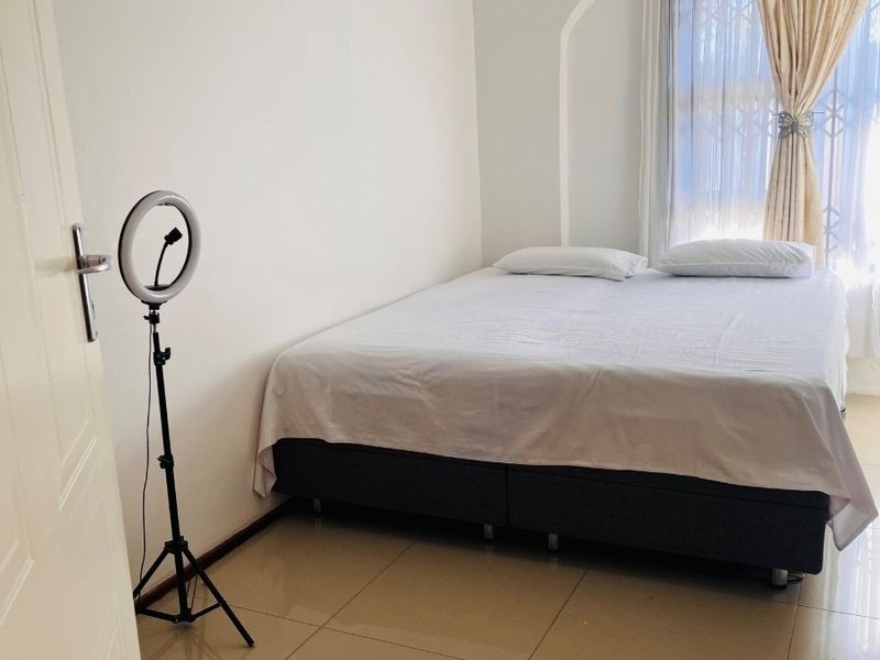 A bedroom featuring tiled flooring and decorative ceiling cornicing, with a window fitted with a security gate.