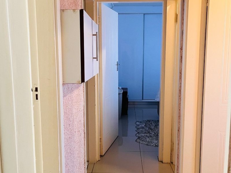 A narrow hallway featuring tiled flooring, coved ceiling detailing, and a built-in wall cabinet, leading towards a bedroom with built-in cupboards.