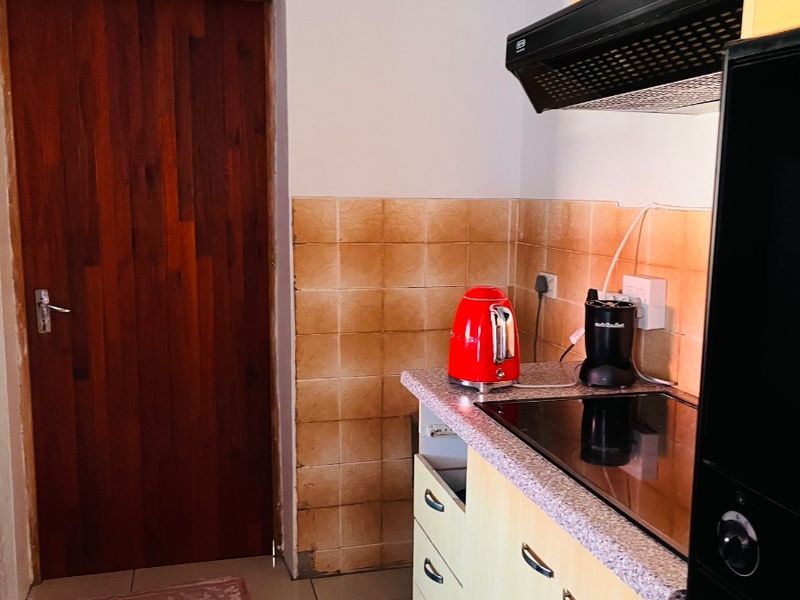 A compact kitchen area featuring built-in cabinetry, a ceramic hob with extractor fan, and tiled splashbacks. The space requires minor repairs and cosmetic updates.