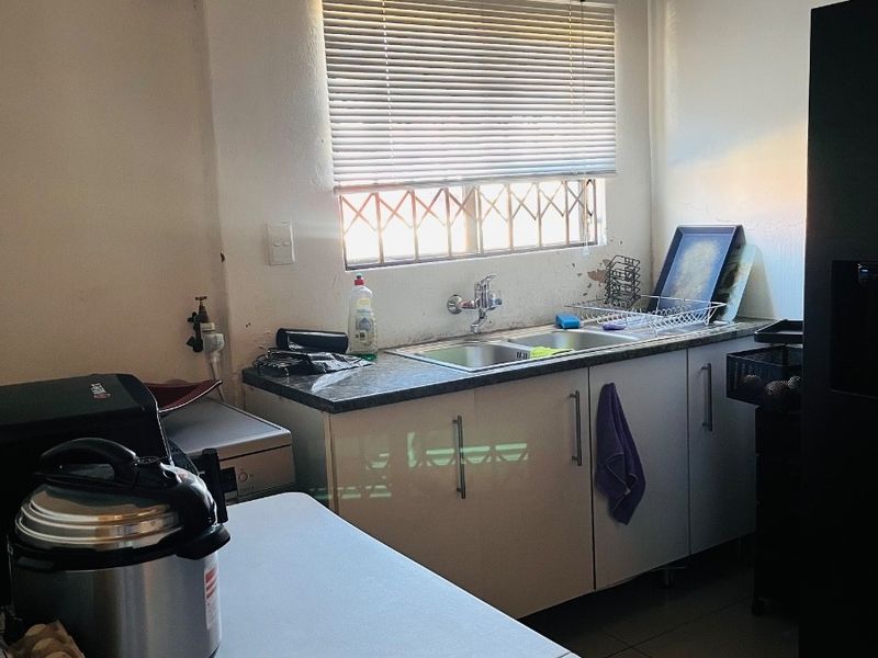 A functional kitchen area featuring base cabinetry, a double bowl sink, and security window bars, requiring cosmetic updates to improve the overall finish.