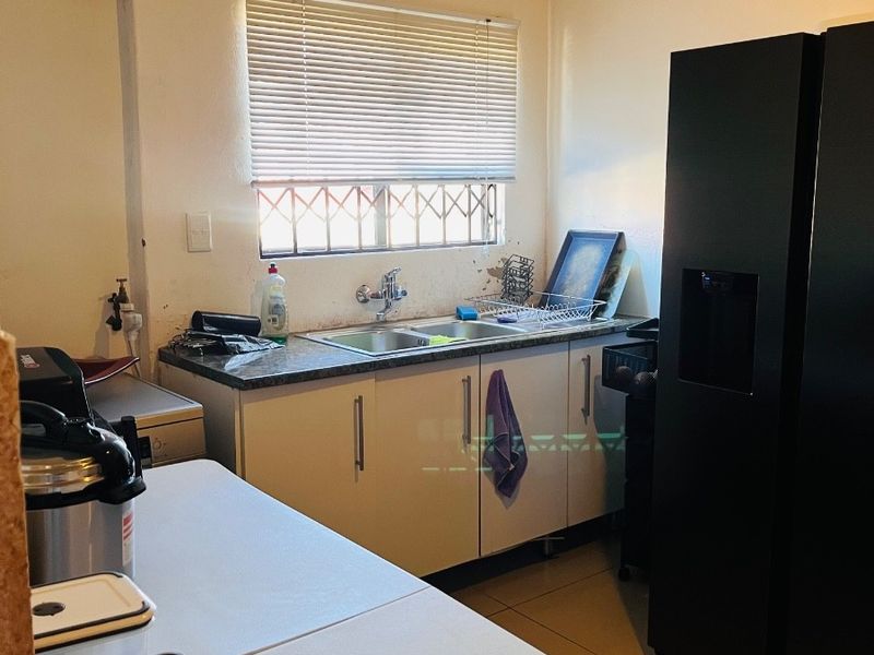A functional kitchen area featuring built-in cabinetry, a double sink, and tiled flooring, currently showing signs of wear and dated finishes.