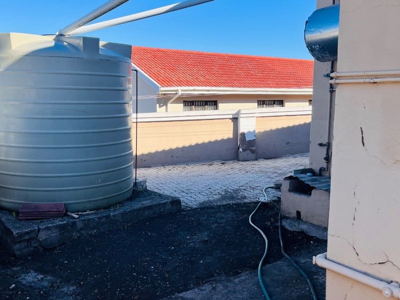 Rear exterior area featuring a water storage tank, paved courtyard, and boundary wall, showing signs of wear and maintenance requirements.