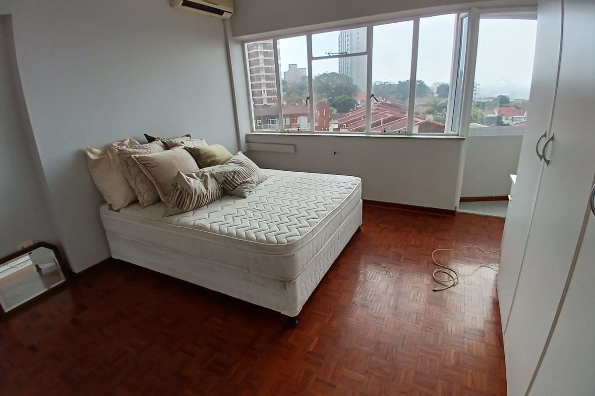 A bedroom featuring parquet flooring, a built-in wardrobe, and a split-system air conditioner, offering natural light and an urban view.