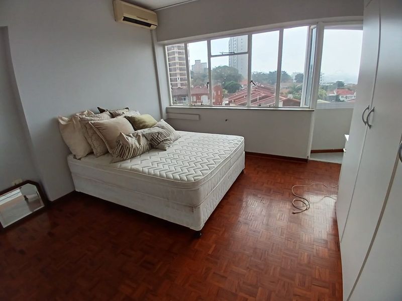 A bedroom featuring parquet flooring, a built-in wardrobe, and a split-system air conditioner, offering natural light and an urban view.
